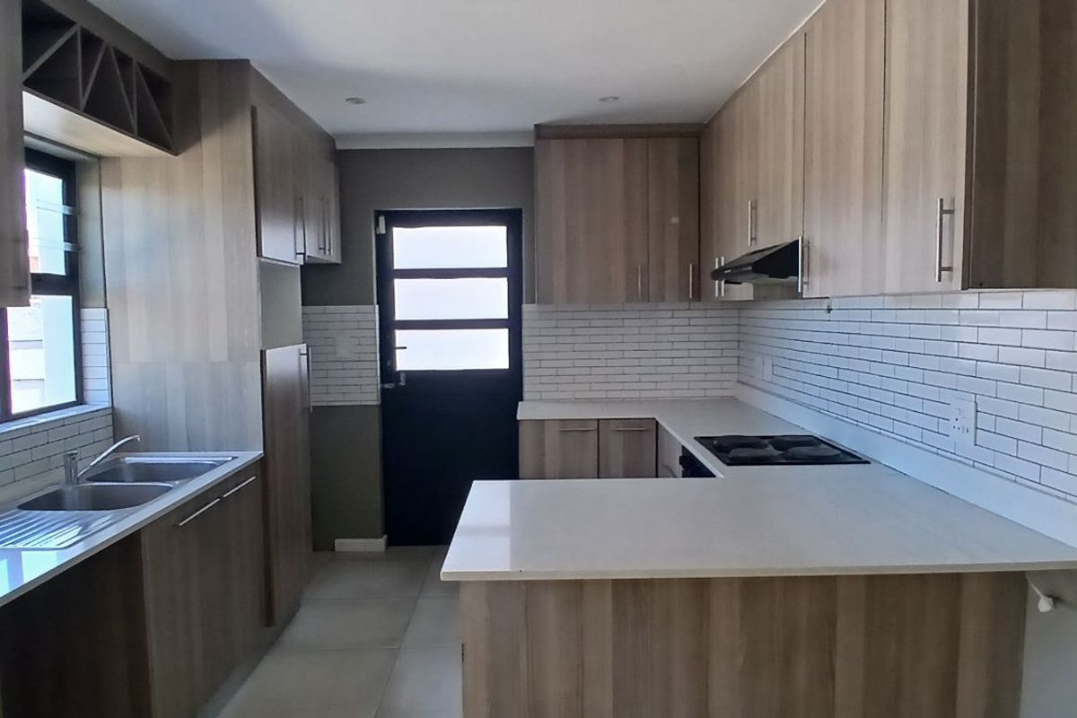 Modern kitchen featuring light wood-grain cabinetry, white stone countertops, subway tile backsplash, integrated hob, and extractor fan.
