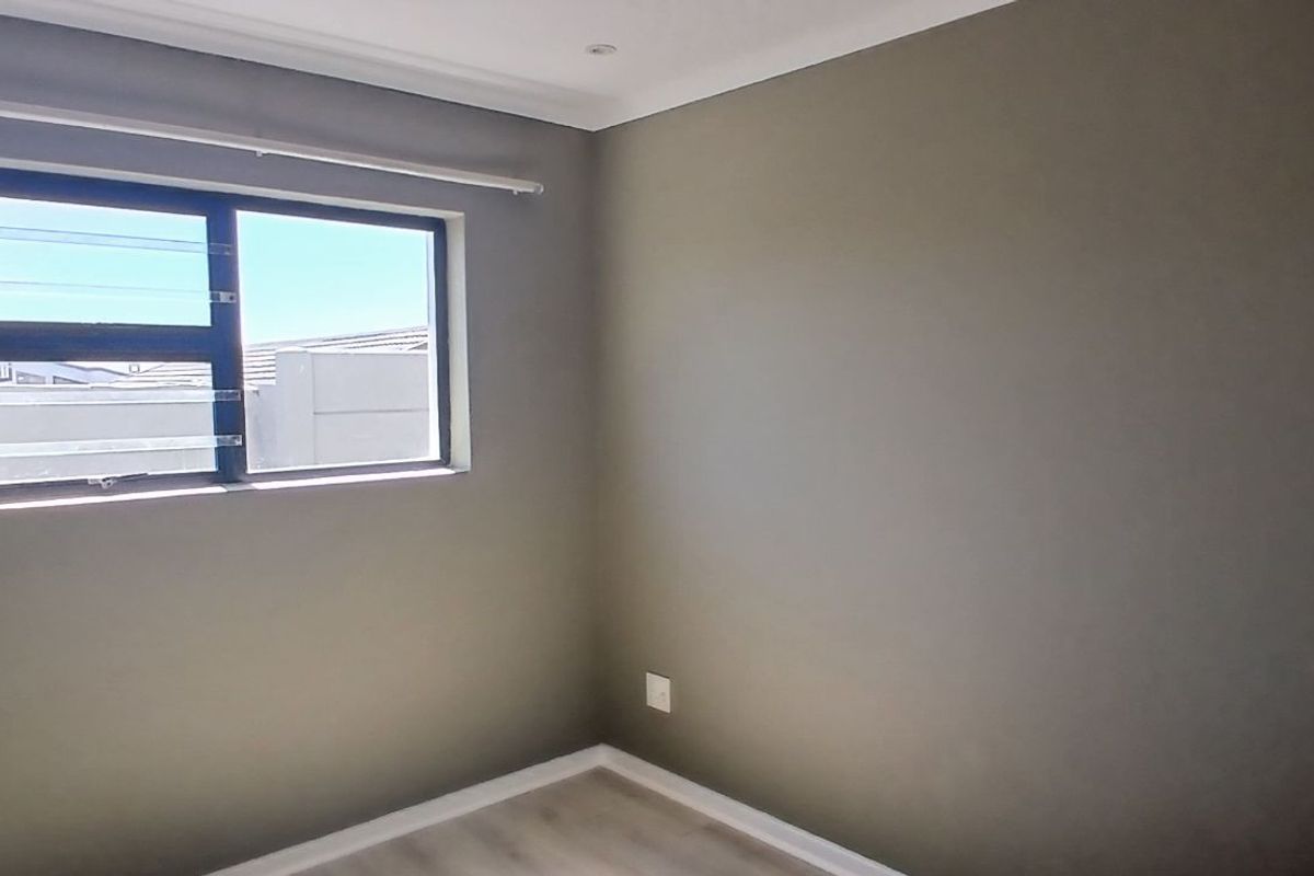 A clean, neutral-toned bedroom featuring modern laminate flooring, a horizontal sliding window, and recessed ceiling lighting.