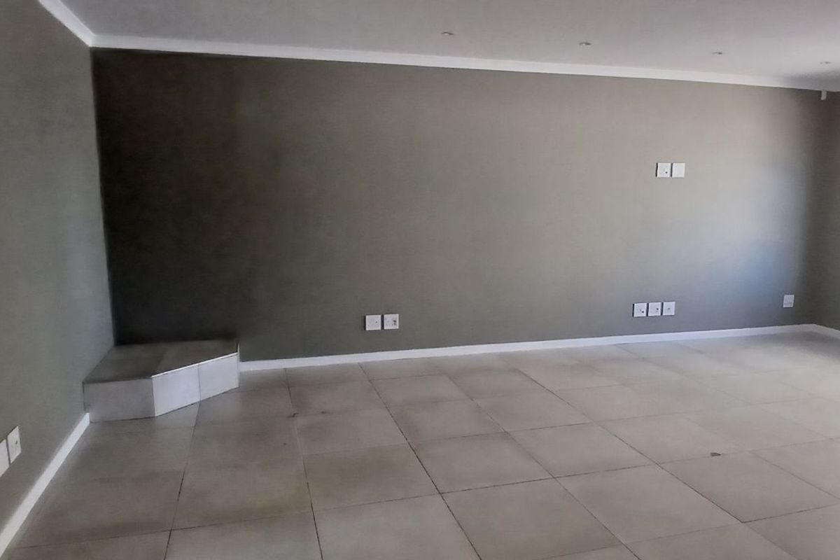 A spacious, empty living area featuring neutral tiled flooring, recessed ceiling lighting, and a built-in corner hearth or display plinth.