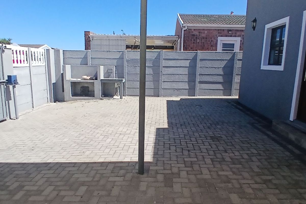 A paved rear courtyard featuring a built-in brick braai, enclosed by high boundary walls, providing a private outdoor space.