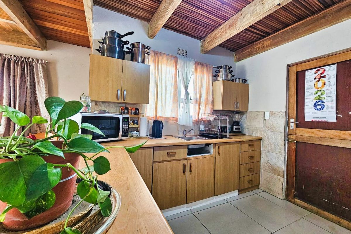 A functional kitchen featuring wooden cabinetry, tiled flooring, and exposed timber ceiling beams, providing a rustic and practical cooking space.