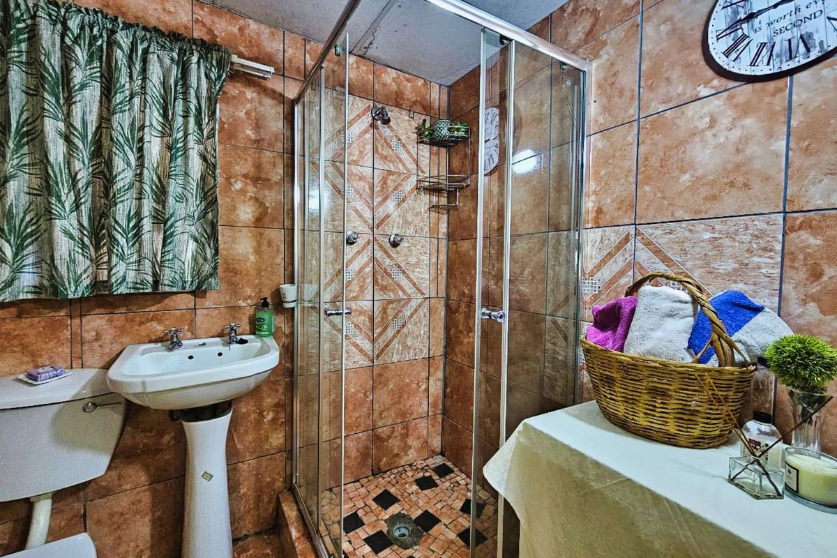 A functional bathroom featuring a glass-enclosed shower, pedestal basin, and toilet, finished with patterned wall and floor tiling.