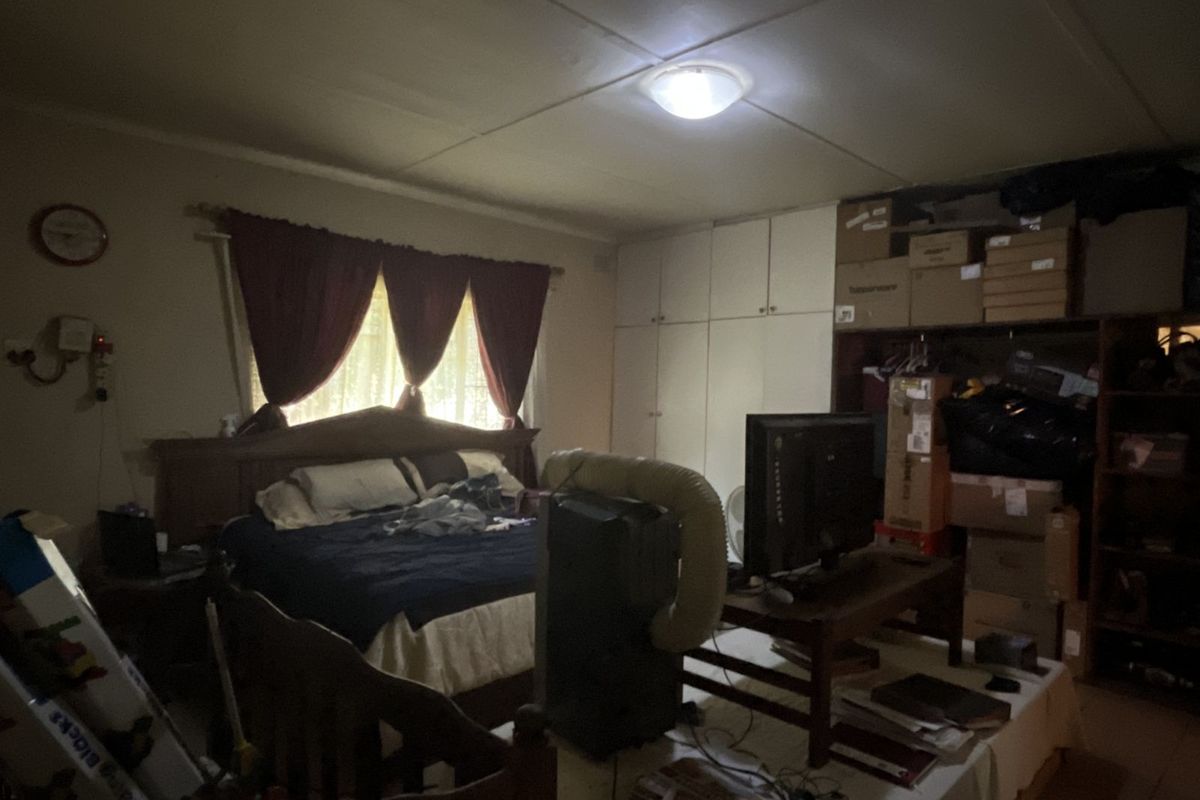 A bedroom featuring built-in storage cupboards and a window with curtain treatments, providing a functional sleeping space with potential for modernization.