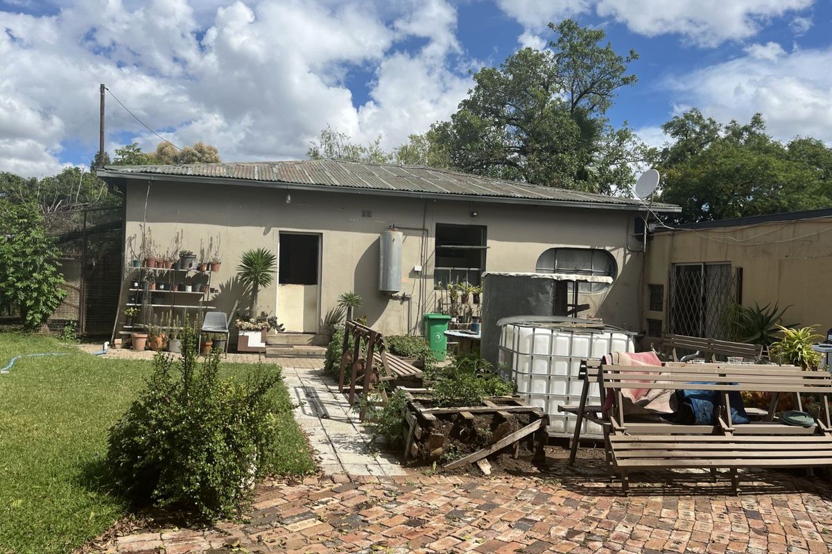 Rear view of the property featuring a corrugated metal roof, brick paved patio area, and access to the garden space.