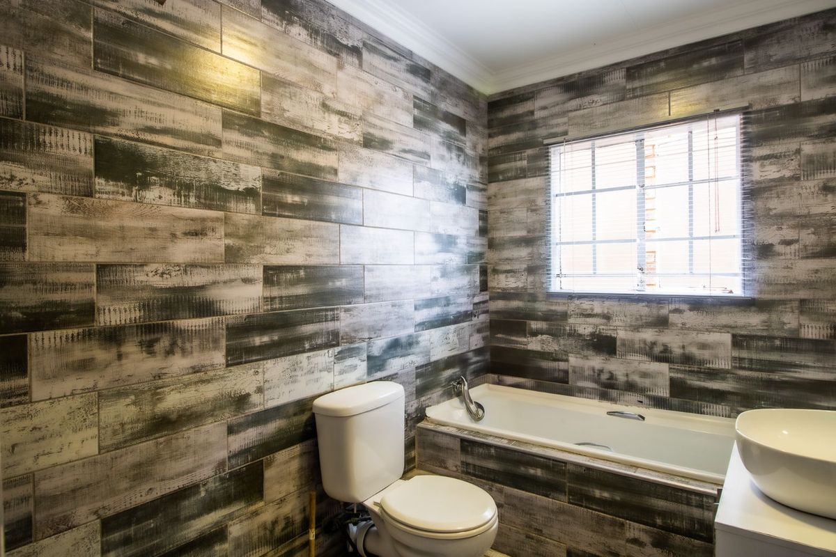 A bathroom featuring wood-look wall tiling, a built-in bathtub, a white ceramic toilet, and a modern vessel sink vanity.