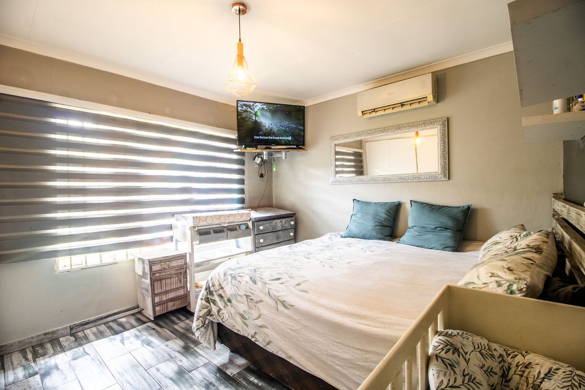 A cozy bedroom featuring wood-look tiled flooring, a wall-mounted air conditioning unit, and modern zebra-style window blinds.