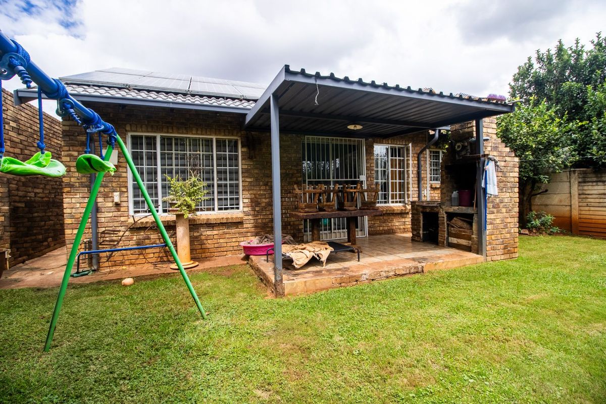 Rear view of the property featuring a covered patio area with a built-in brick braai, overlooking a private garden space.