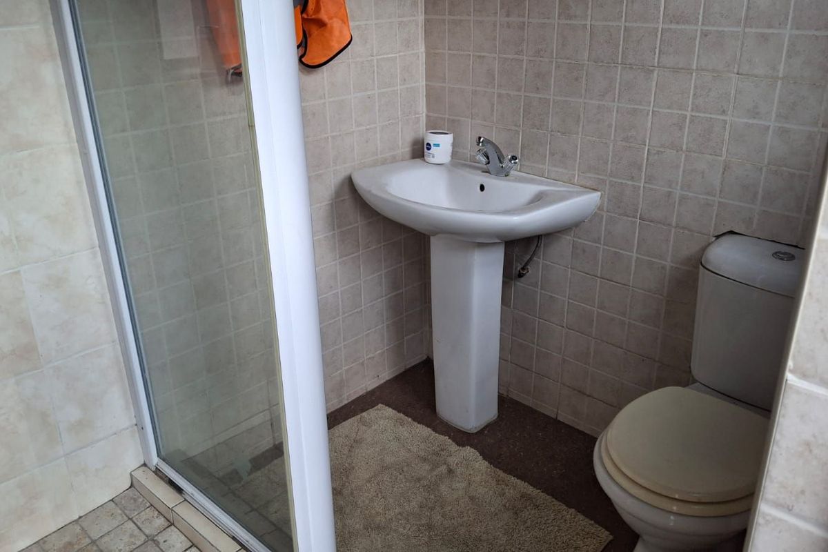 A functional bathroom featuring a pedestal basin, a standard toilet, and a glass-enclosed shower with neutral wall tiling.
