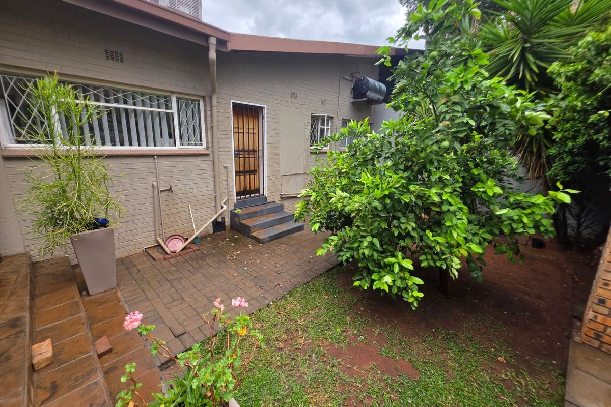 Rear exterior view of the property featuring a paved patio area, established garden, and direct access to the home via a security door.