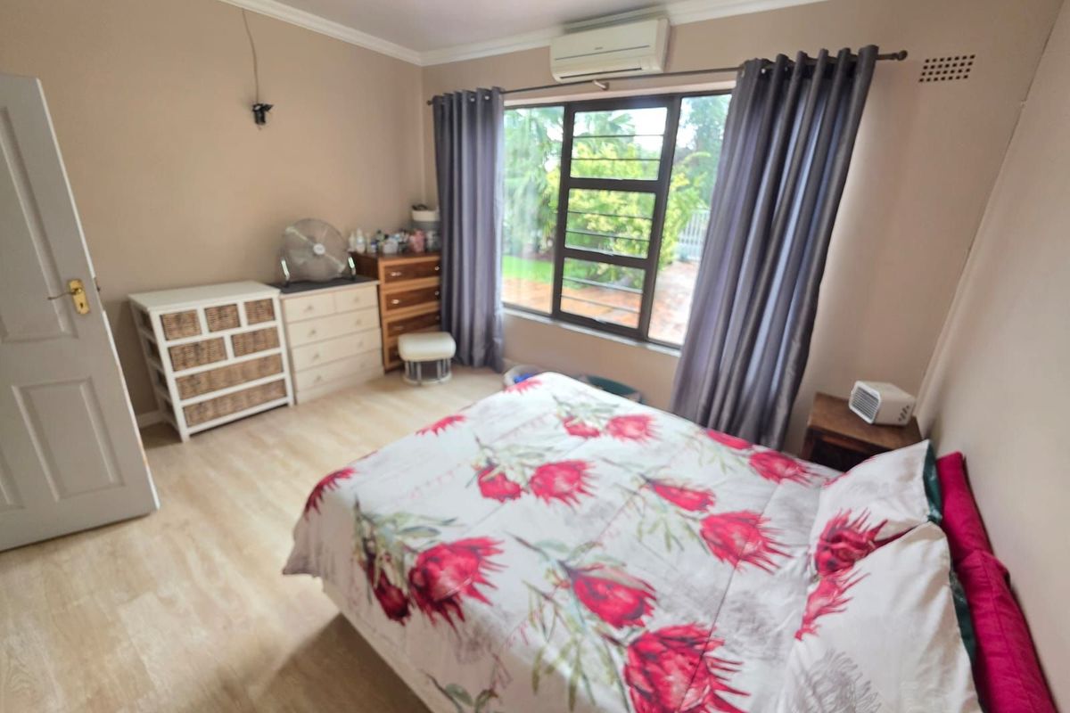 A bedroom featuring light wood-look flooring, a wall-mounted air conditioning unit, and a large window with garden views.
