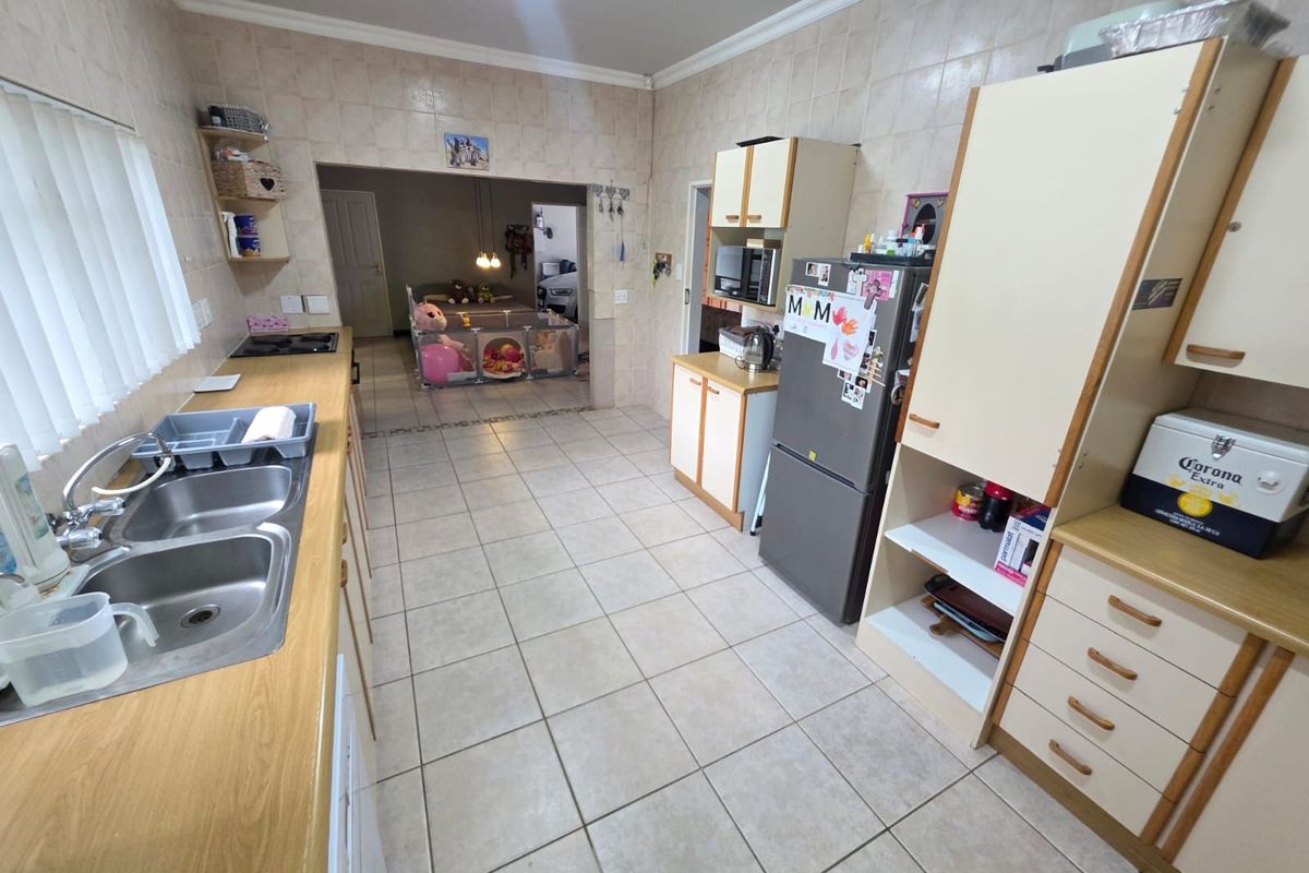A functional kitchen featuring tiled walls and flooring, ample built-in cabinetry, and a double basin sink, with an open-plan layout leading to an adjacent room.