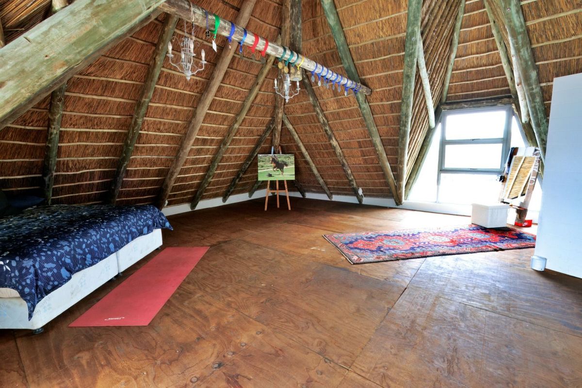 Spacious attic-style bedroom featuring a high vaulted thatch ceiling with exposed timber beams and large windows providing natural light.
