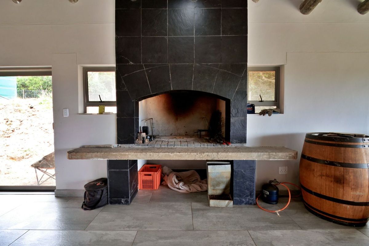 Indoor braai area featuring a large built-in fireplace with black tile surround and a concrete prep counter, set against a neutral tiled floor.