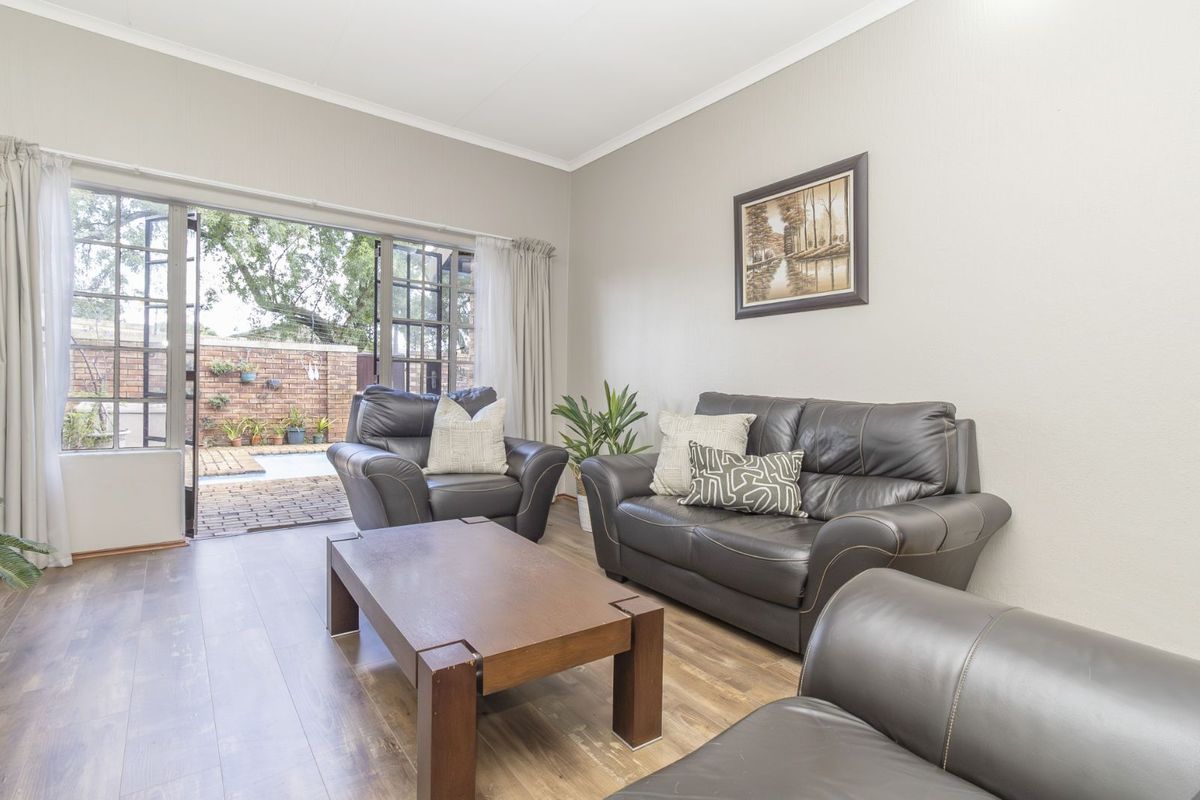 A bright living room featuring wood-look laminate flooring and large glass doors opening onto a private patio area.