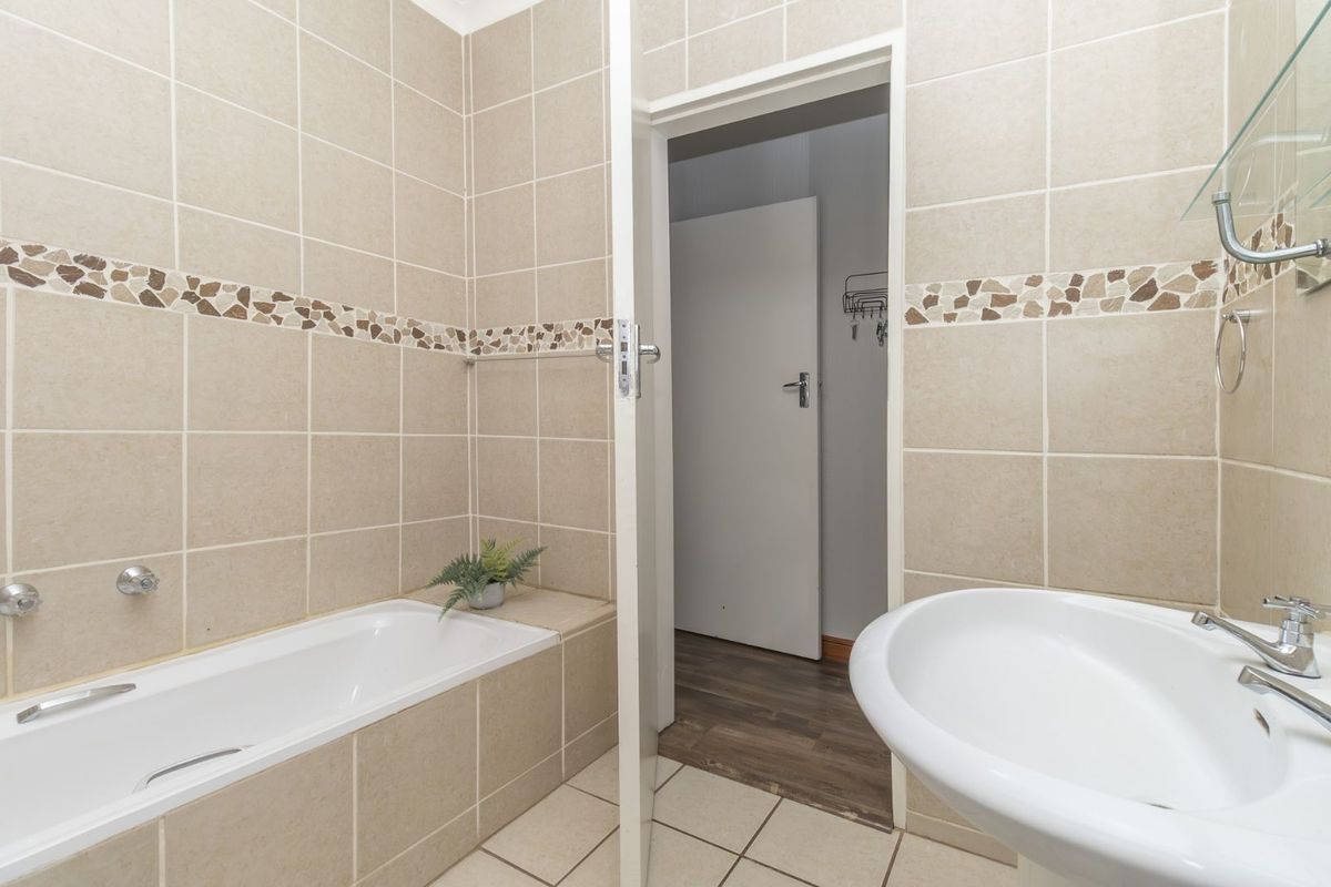 A functional bathroom featuring a tiled bathtub surround, pedestal basin, and neutral wall tiling with a decorative mosaic border.