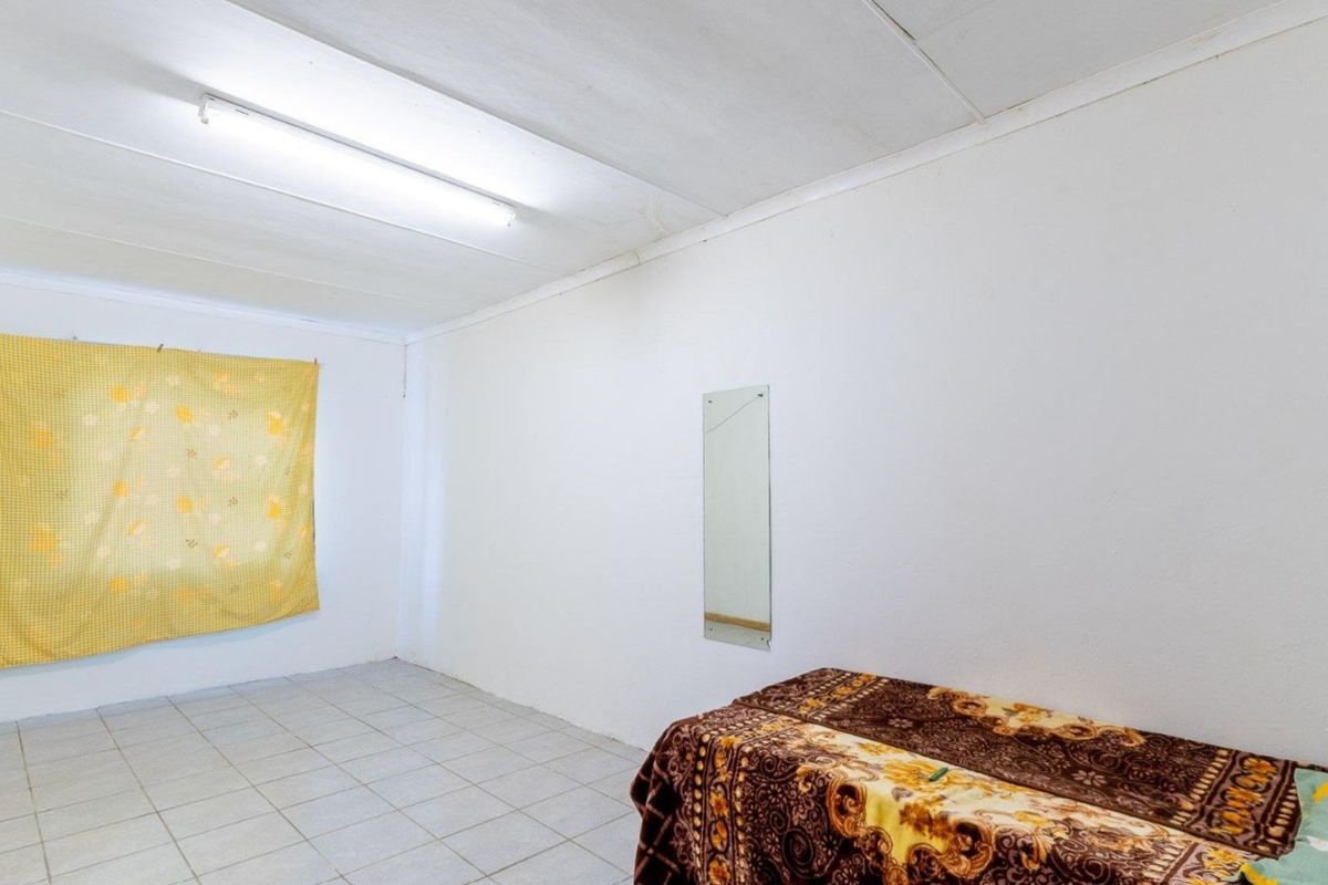 A simple bedroom featuring tiled flooring, a plain ceiling with a fluorescent light fixture, and a wall-mounted mirror.