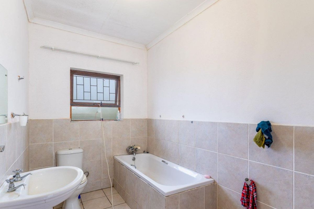 A functional bathroom featuring a standard bathtub, pedestal basin, and toilet with neutral wall tiling and a security-barred window.