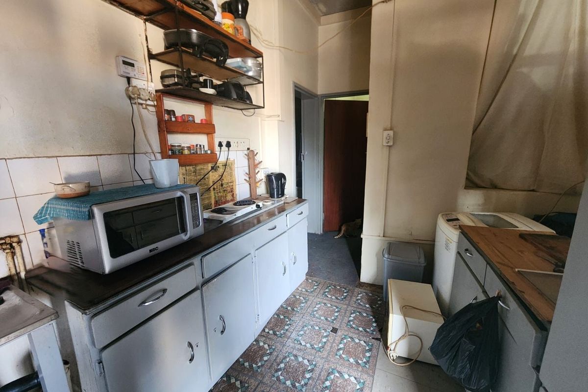 A dated kitchen area featuring basic cabinetry, tiled flooring, and wall-mounted shelving, requiring significant renovation and modernization.
