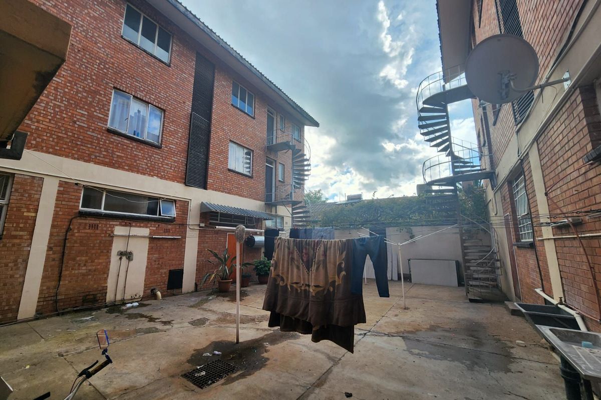 Rear courtyard area featuring brick building facades, external spiral staircases, and concrete paving, providing functional outdoor space for the property.