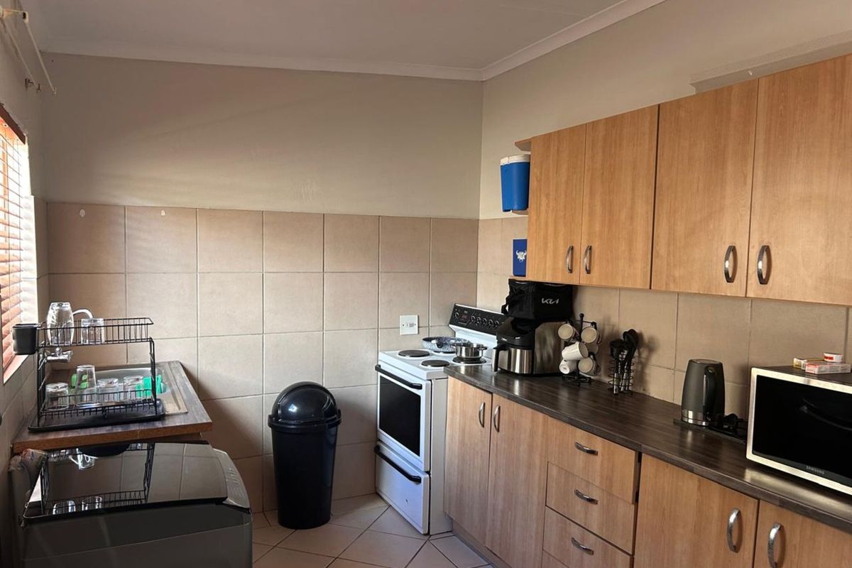 A functional kitchen featuring light wood cabinetry, tiled splashbacks, tiled flooring, and a freestanding electric stove.