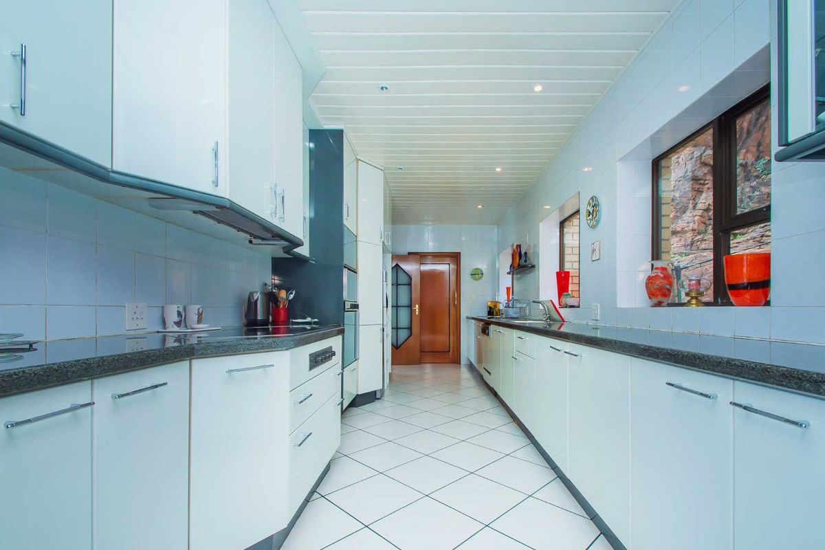 A galley-style kitchen featuring white cabinetry, dark granite countertops, tiled flooring, and a tongue-and-groove ceiling.