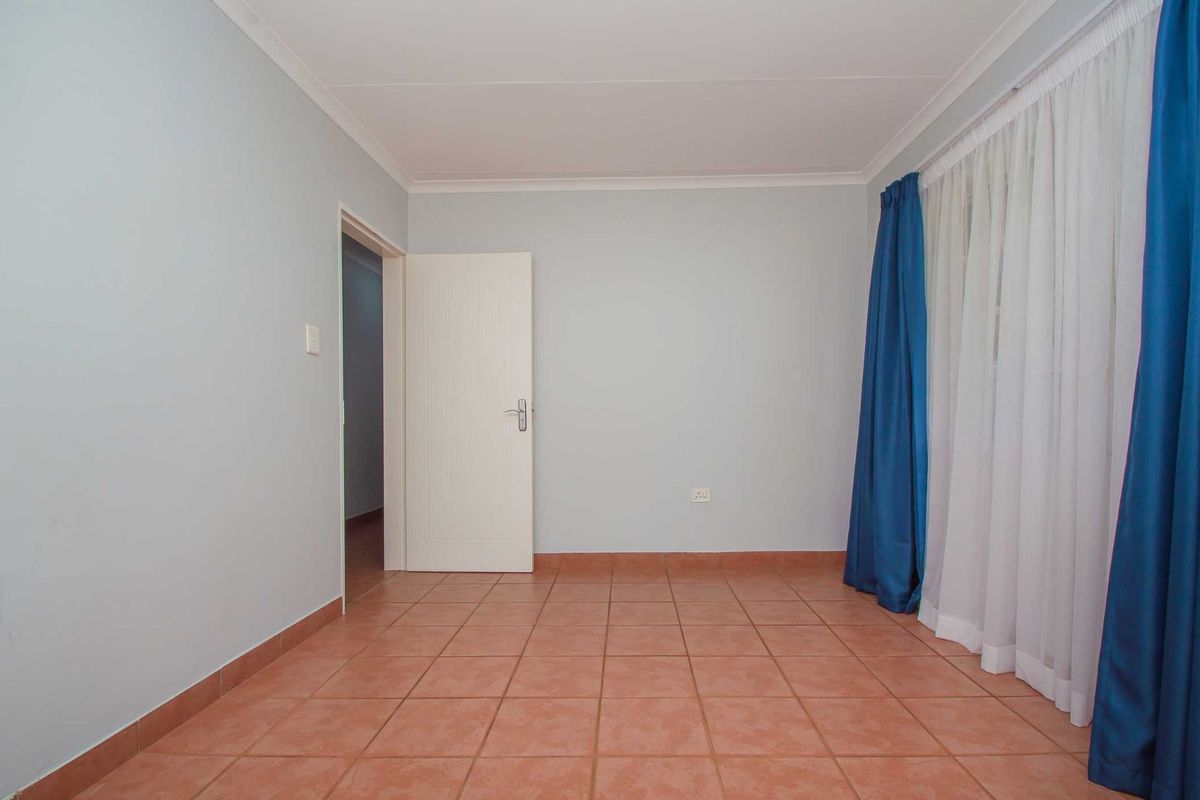 A clean, empty bedroom featuring neutral wall paint, terracotta floor tiles, and a standard interior door.