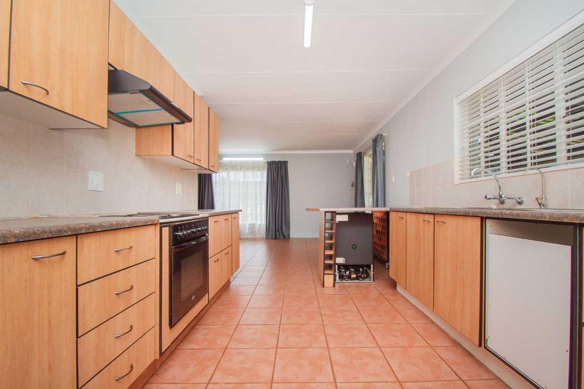 A functional galley-style kitchen featuring light wood-tone cabinetry, tiled flooring, a built-in oven with extractor fan, and a double sink setup.