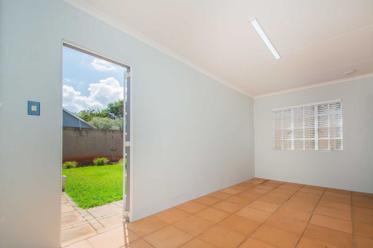 A bright, empty room featuring tiled flooring, a fluorescent ceiling light, and direct access to the rear garden through a glass-paneled door.