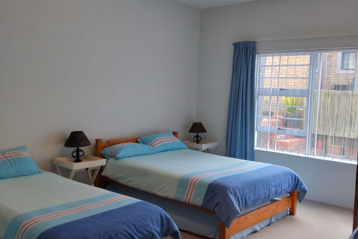 A spacious bedroom featuring a ceiling fan, neutral carpeting, and a window with security bars overlooking the exterior.