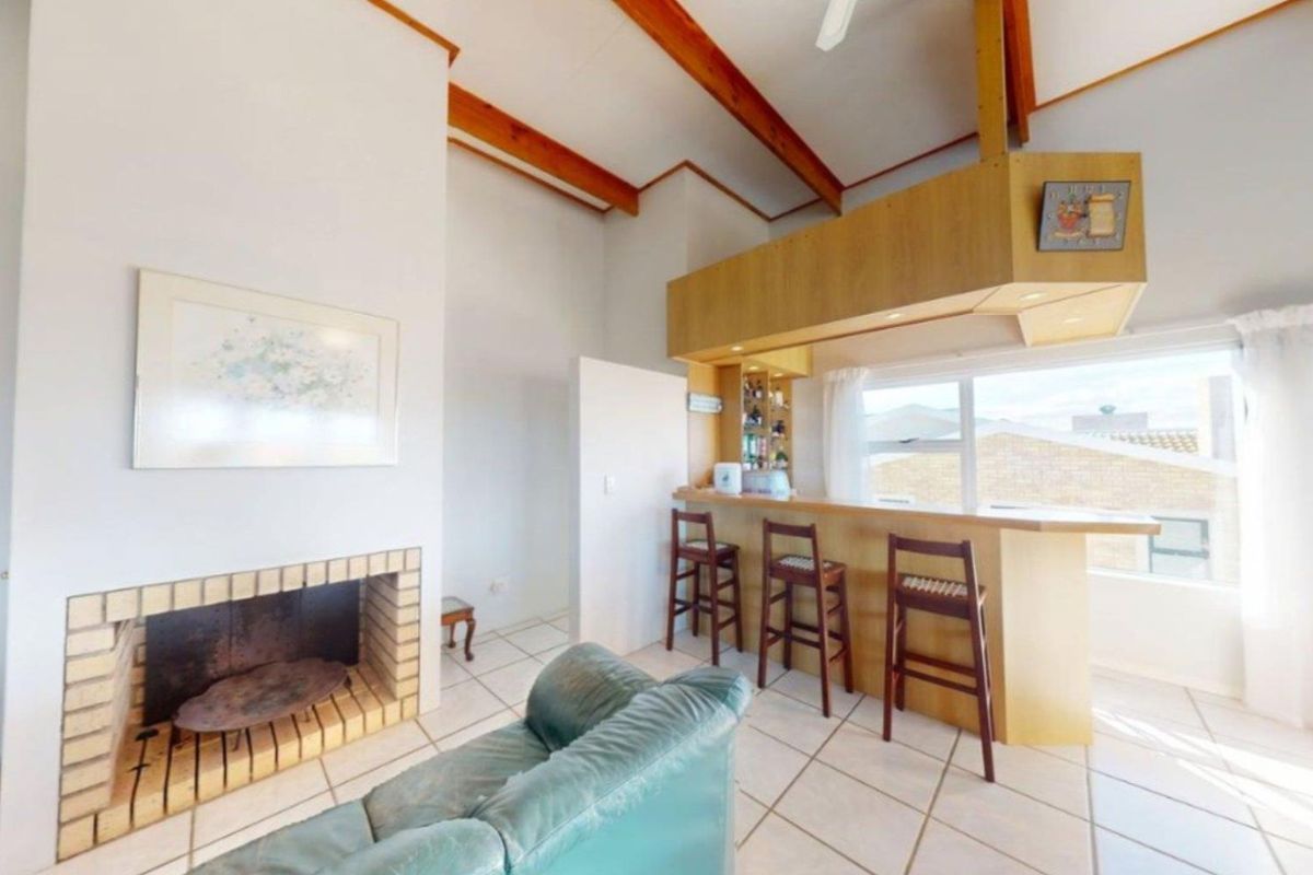 Spacious living area featuring a high vaulted ceiling with exposed timber beams, a brick fireplace, and a built-in wooden bar counter.