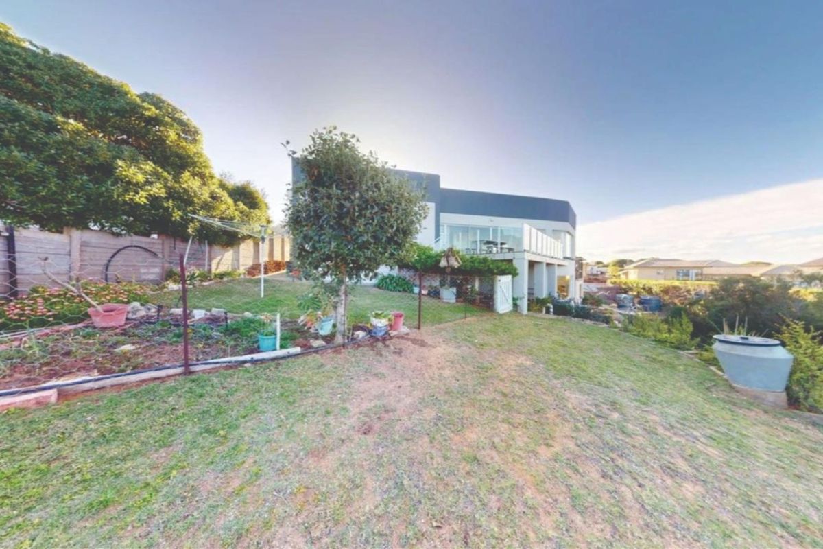 A view of the rear garden and backyard area, featuring a lawn, perimeter fencing, and a raised patio deck attached to the main house structure.