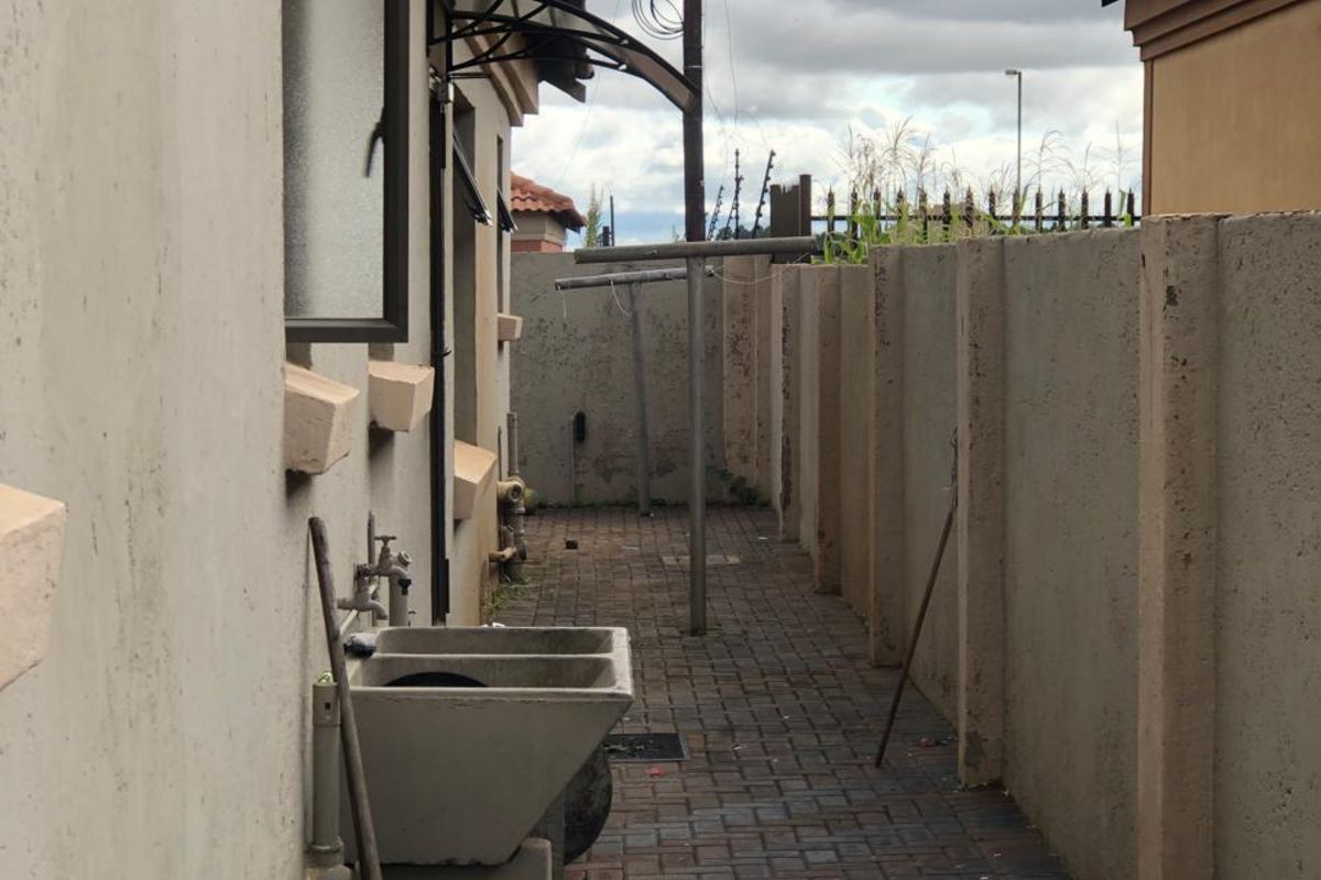 A narrow side exterior area featuring paved flooring, a fixed concrete utility sink, and a metal washing line structure.