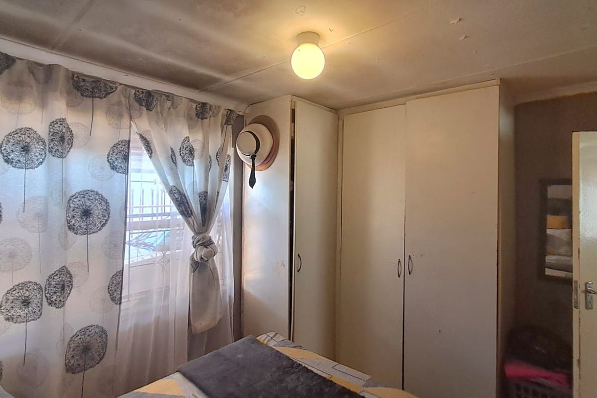 A bedroom featuring built-in cupboards and a ceiling light fixture, showing signs of wear on the ceiling surface.