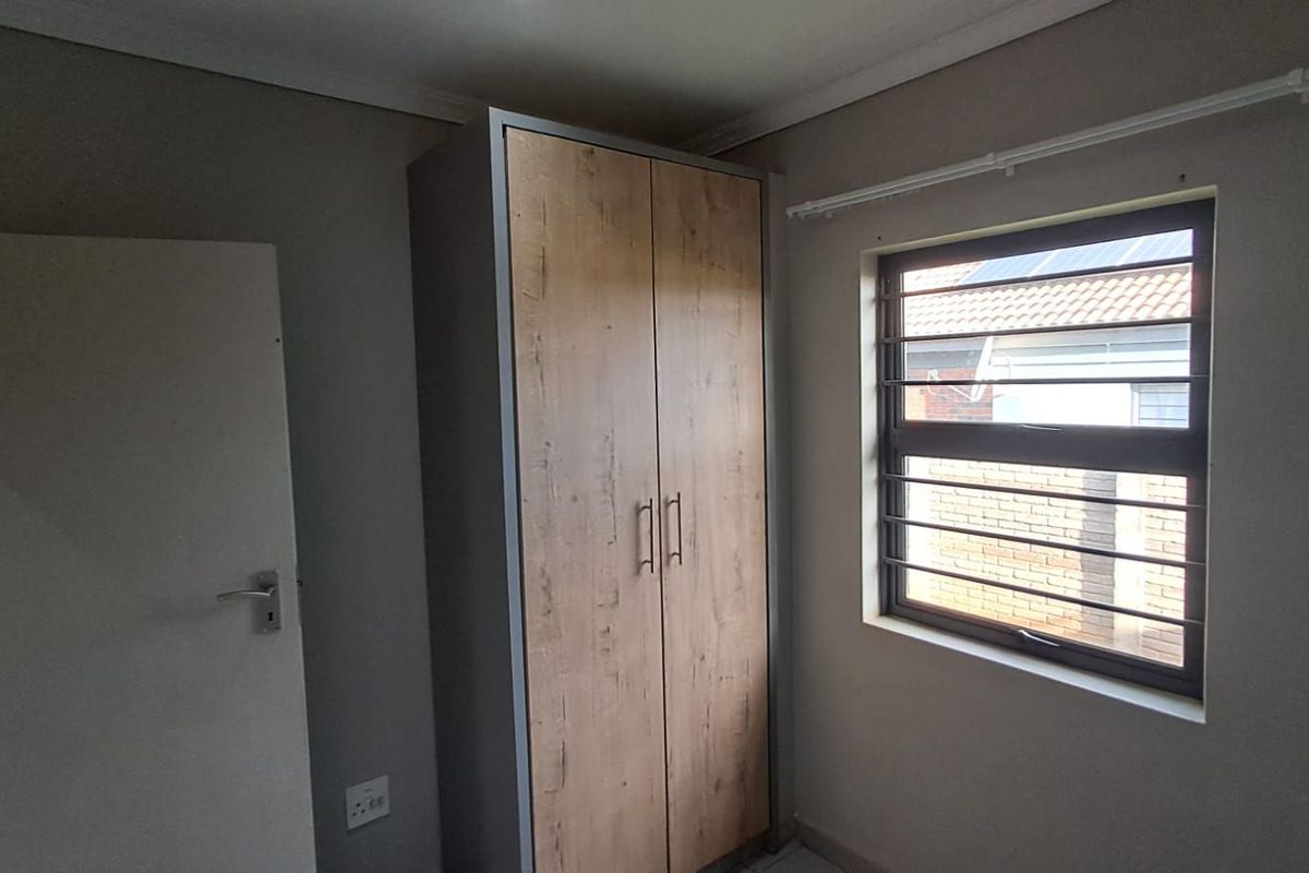 A clean, empty bedroom featuring a modern wood-finish built-in wardrobe and a window fitted with security bars.