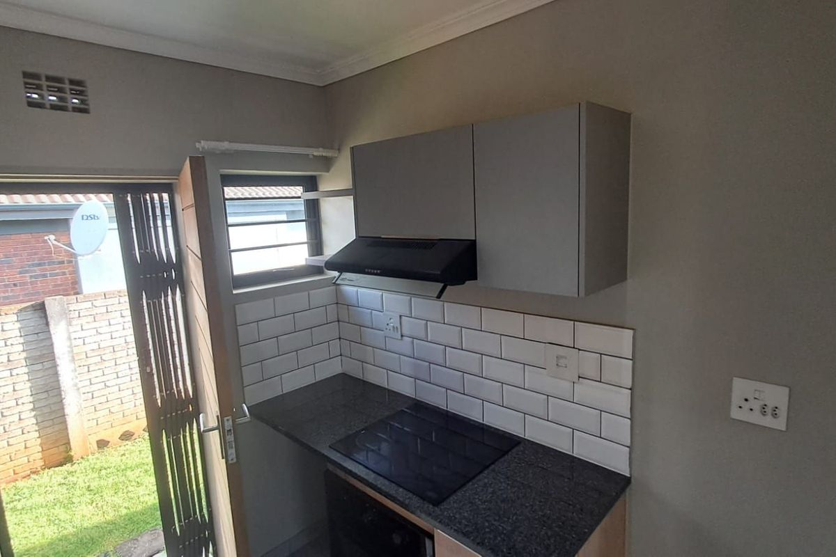 Compact kitchen featuring modern subway tile backsplash, stone countertops, built-in oven, electric hob, and extractor fan with direct access to the rear garden.