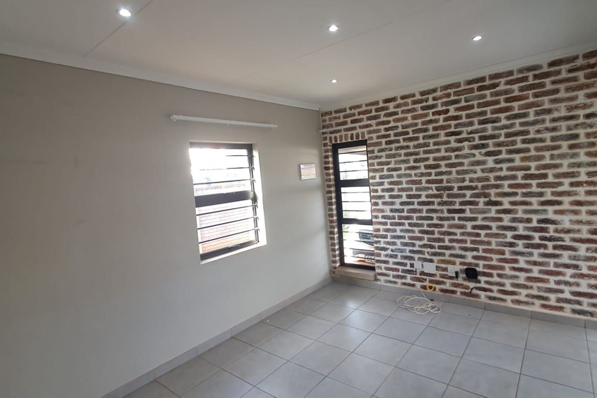An empty living area featuring a rustic exposed brick feature wall, neutral tiled flooring, and recessed downlighting, providing a clean and versatile space.