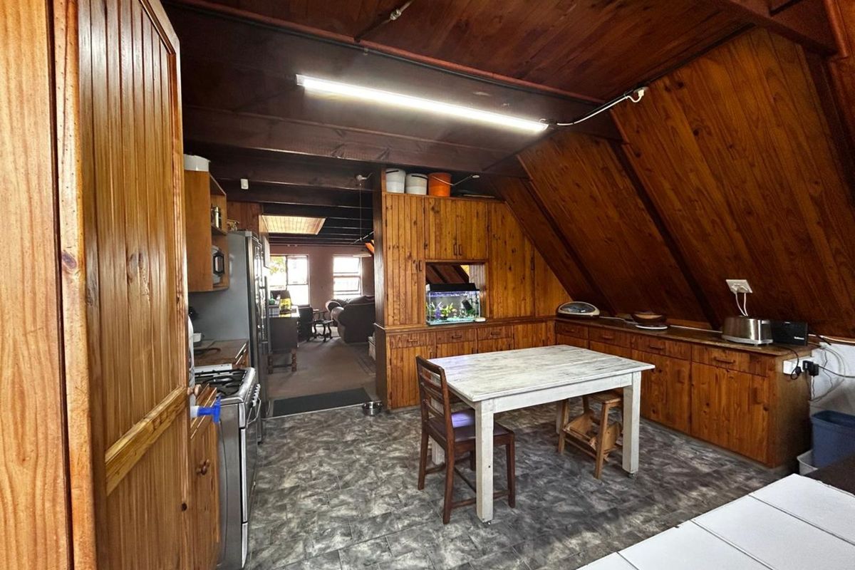 A rustic kitchen featuring extensive timber wall and ceiling paneling, built-in wooden cabinetry, and a tiled floor, with an open-plan layout leading to the living area.