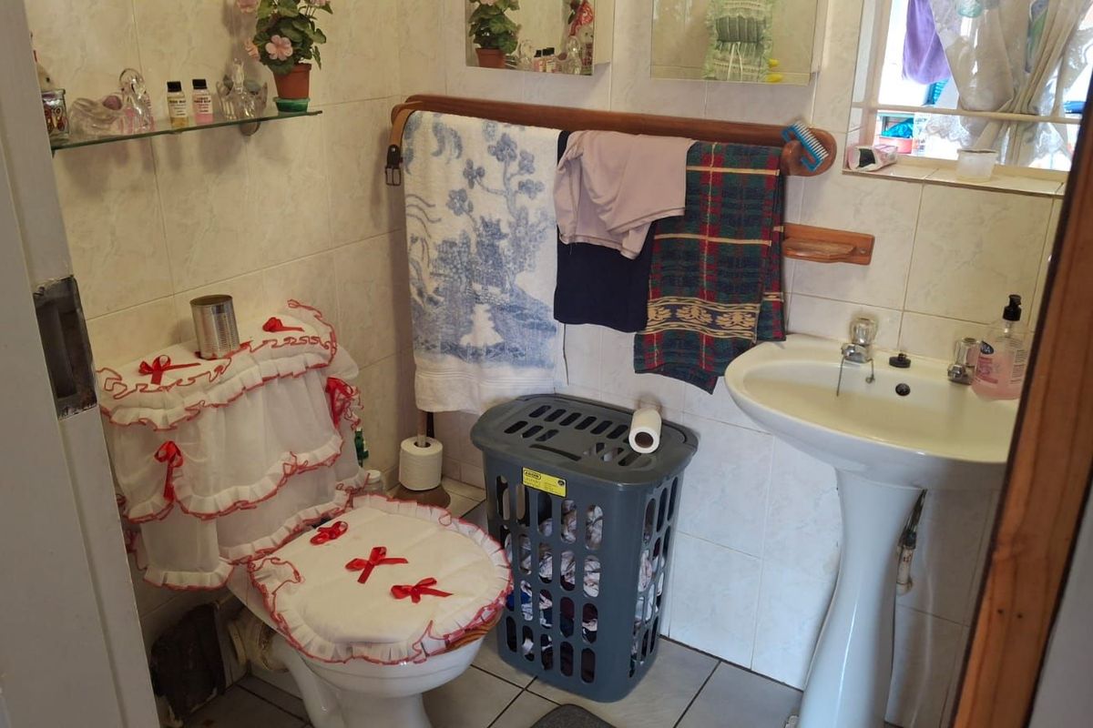 A functional bathroom featuring a pedestal basin, toilet, and wall-mounted shelving, finished with neutral wall tiles.