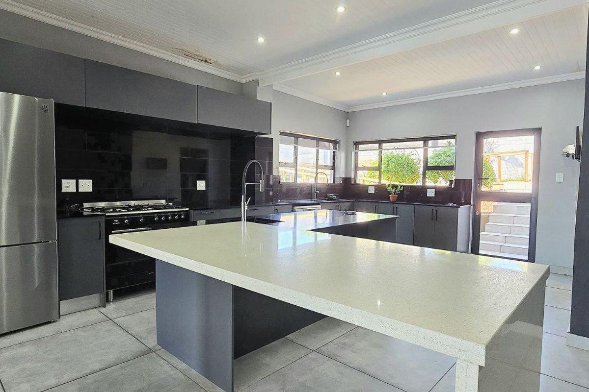 Modern kitchen featuring dark cabinetry, stone countertops, a central island, and tiled flooring with direct access to the exterior.