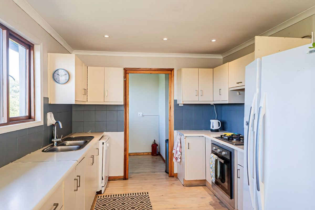 Functional kitchen featuring built-in cabinetry, integrated oven and hob, double sink, and tiled splashbacks, with direct access to an adjoining utility area.