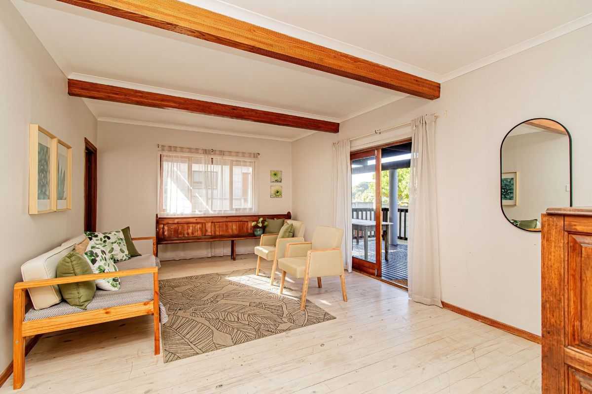 A bright living room featuring exposed timber ceiling beams, light-toned timber flooring, and sliding glass doors providing access to an outdoor patio area.
