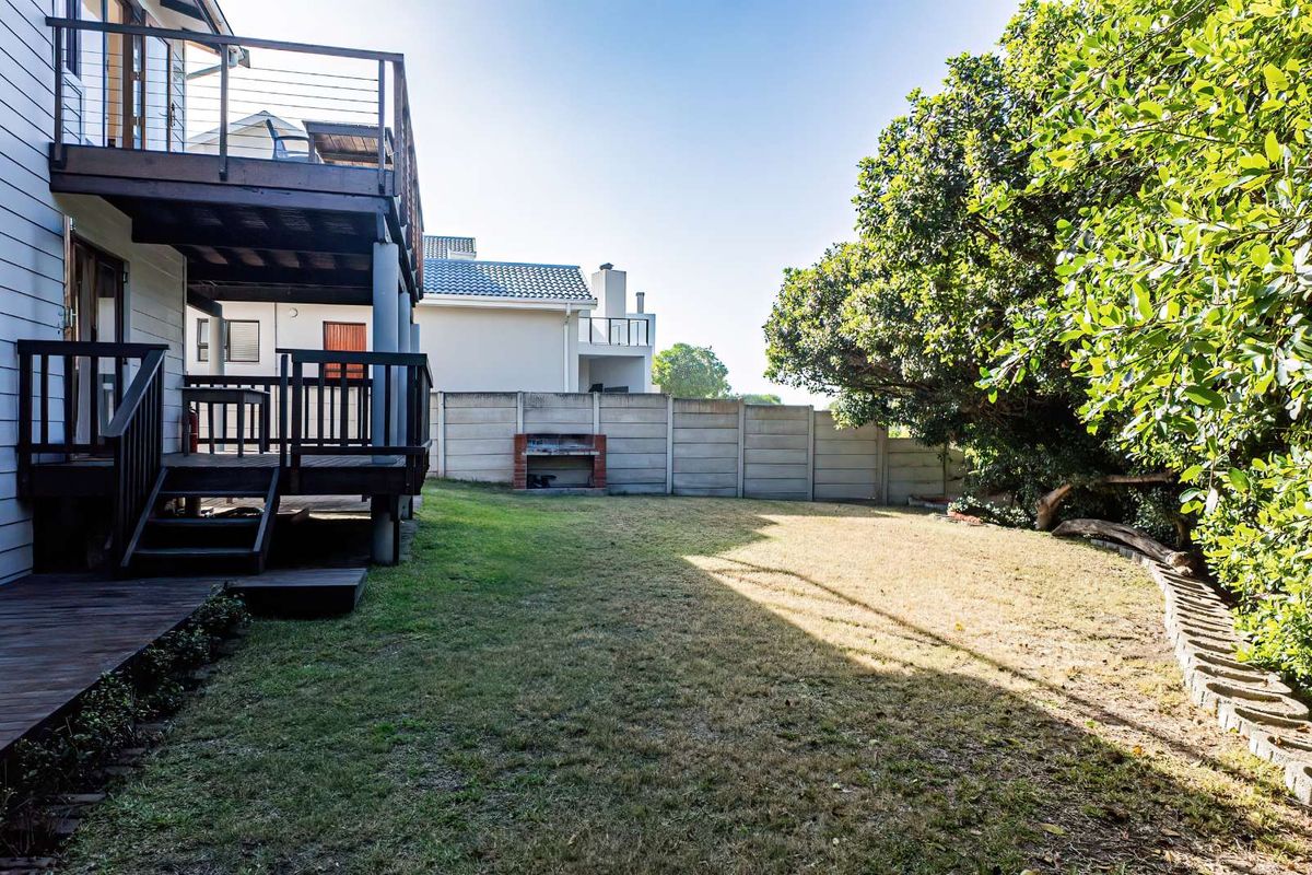 A spacious rear garden featuring a multi-level timber deck, built-in brick braai area, and perimeter concrete walling.