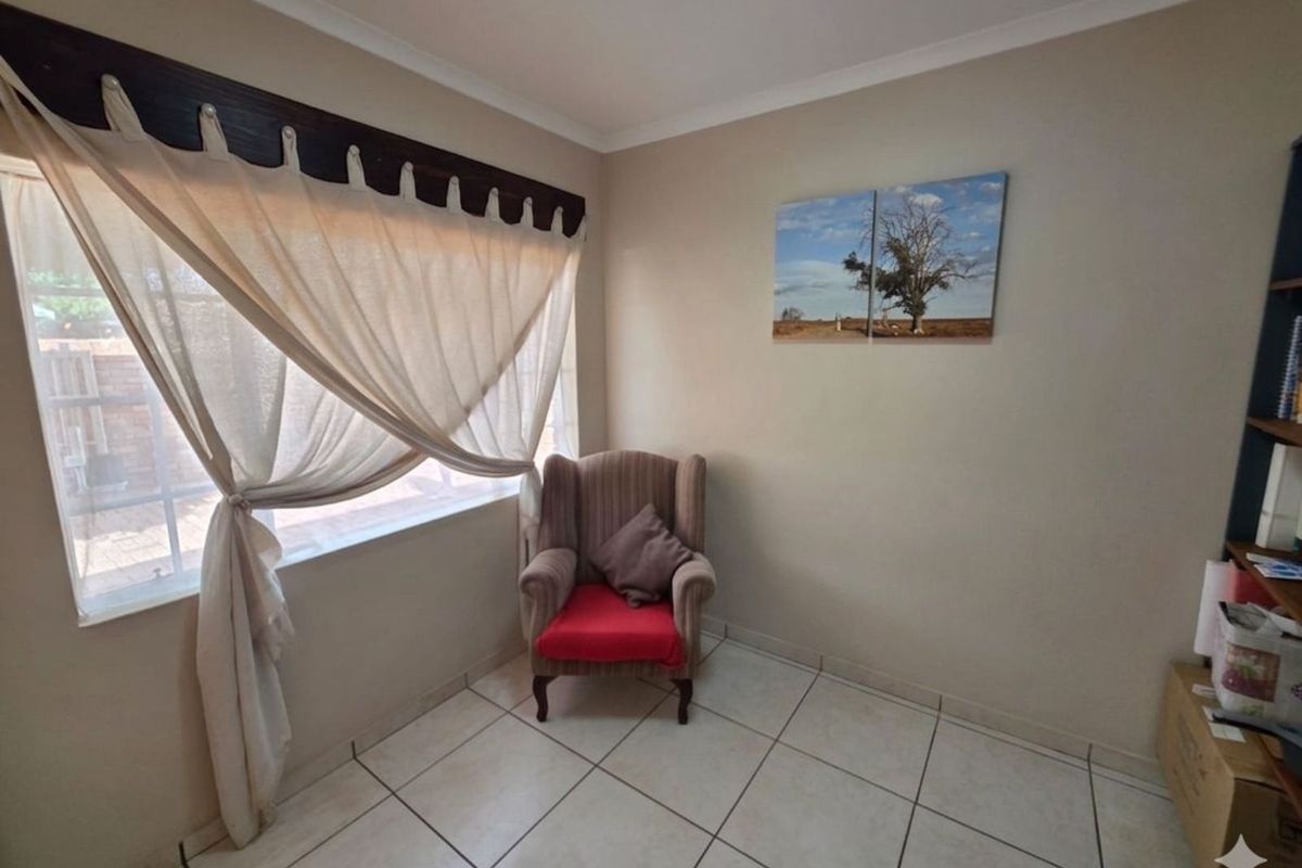 A simple living area featuring neutral wall tones, tiled flooring, and a large window with decorative pelmet.