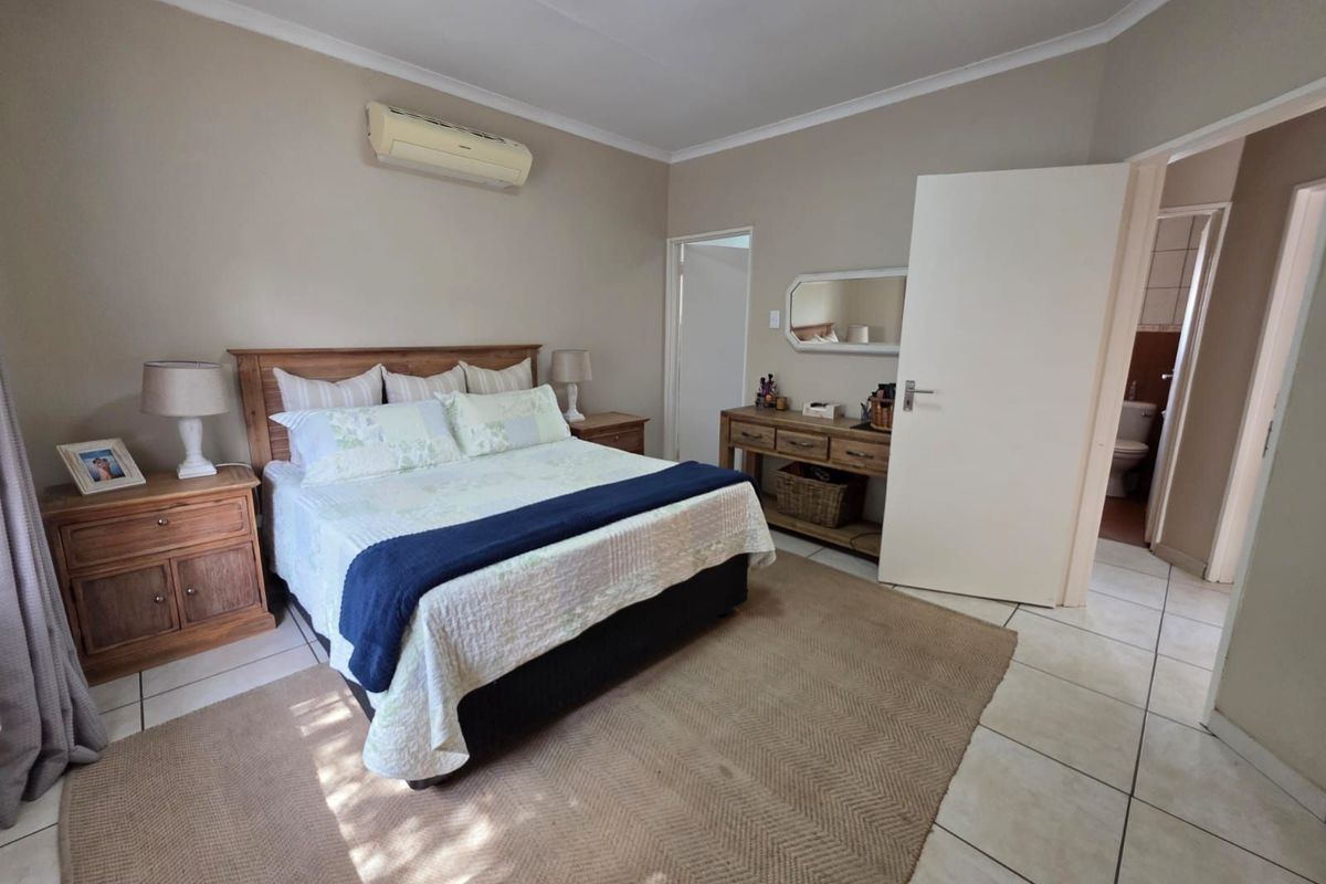A spacious bedroom featuring tiled flooring, a wall-mounted air conditioning unit, and an en-suite bathroom access.