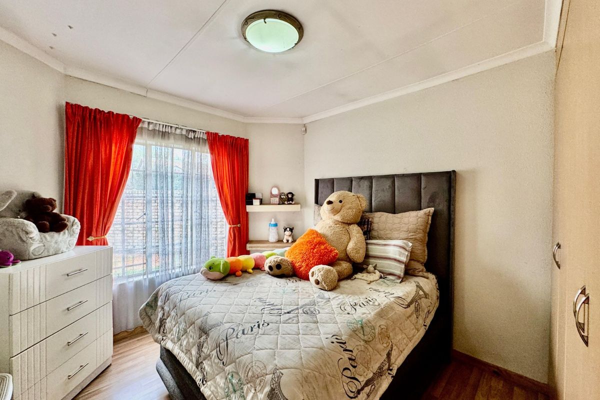 A cozy bedroom featuring laminate flooring, built-in wardrobe cabinetry, and a window with curtain tracks.