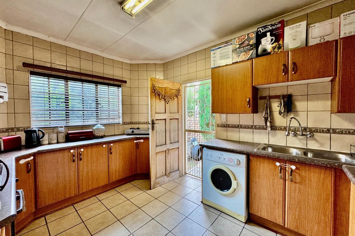 A functional kitchen featuring wood-look cabinetry, tiled splashbacks, a stainless steel sink, and direct access to an exterior door.