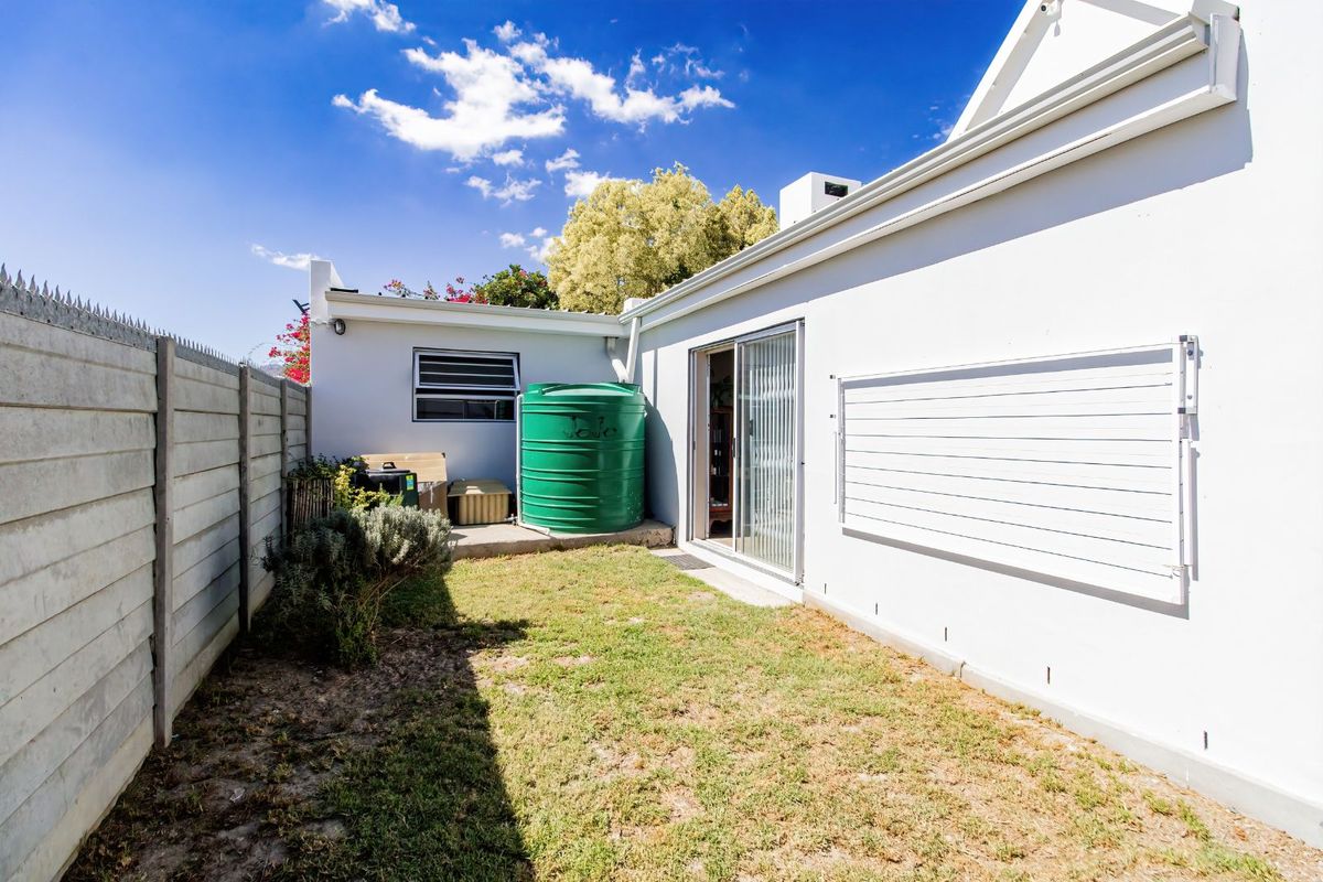 A private rear garden area featuring a green water storage tank, a wall-mounted drying rack, and sliding door access to the home.