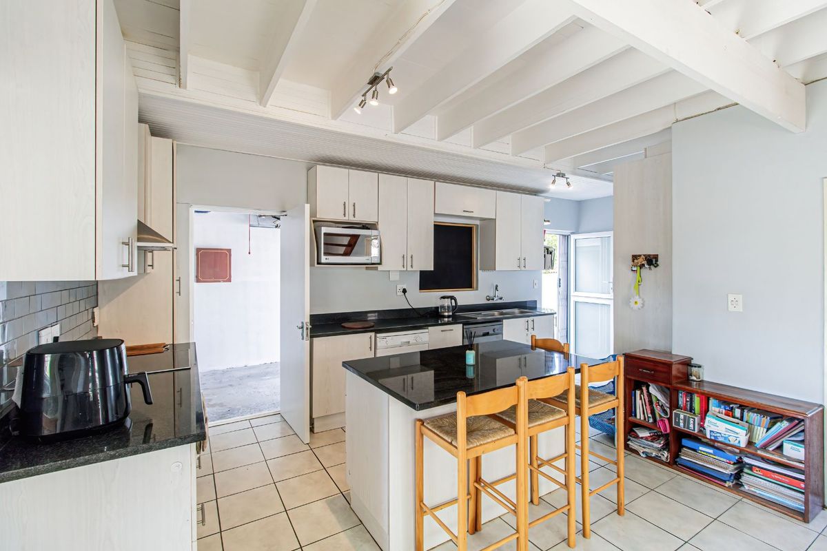A functional kitchen featuring white cabinetry, dark granite countertops, a central island with breakfast bar seating, and exposed white ceiling beams.