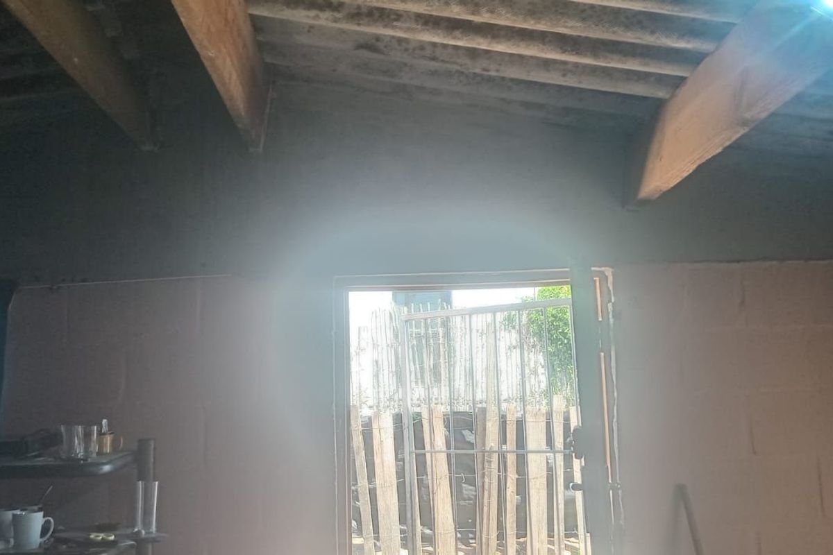 Interior view of a room featuring exposed timber roof beams and unfinished blockwork walls, leading to an exterior doorway.