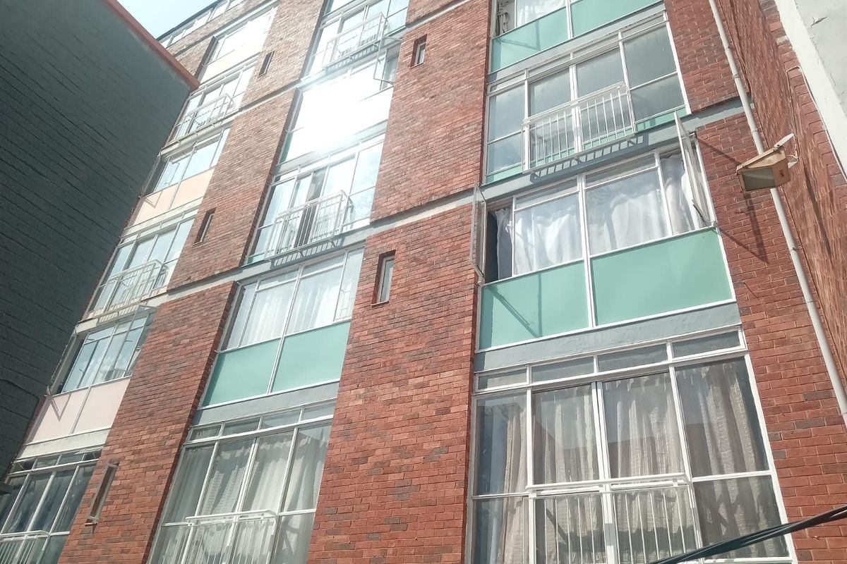Exterior view of a multi-story apartment building featuring a red brick facade with integrated balconies and large glass windows.